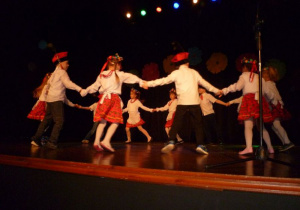12 dzieci tańczy w kole trzymając się za ręce;