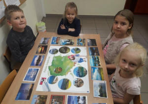 Karol, Lena, Zosia i Julia oglądają mapę Polski i dopasowują do regionów widokówki.