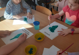 Milena i Oliwia malują farbami w kolorze zielonym kontynenty.