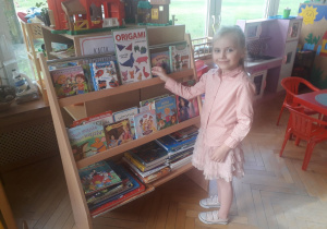 Milenka wybiera książeczkę do przeczytania z przedszkolnej biblioteczki.