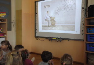 Przedszkolaki poznają etapy powstania książki oglądając na tablicy interaktywnej film edukacyjny „Jak powstaje książka”.
