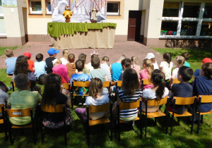 Dzieci z grupy "Biedronek" i "Misiaczków" oglądają w ogrodzie bajkę.