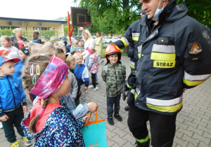 Tymon przymierza kask strażacki, a Wiktorka i Lidzia w imieniu wszystkich przedszkolaków dziękują serdecznie strażakom za przemiłe spotkanie.