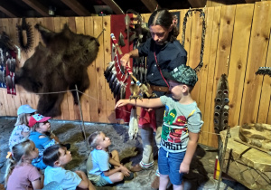 Oskar wraz z panem Krzyśkiem prezentują dzieciom laskę ze szponami orła wykorzystywaną podczas tańców Indian.