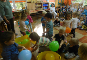 Dzieci z grupy Biedronek szukają wesołe i smutne baloniki, wkładają je do oznaczonych buźką wesołą i smutną pojemników.