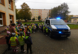 Przedszkolaki w ogodzie przedszkolnym przy samochodzie policyjnym.