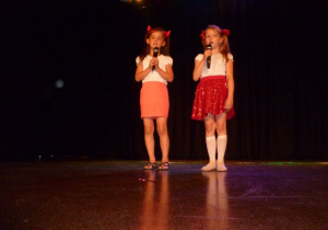 Jagna i Nikola stoją na scenie, trzymając mikrofony bezprzewodowe deklamują wiersz;