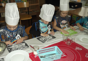Sara, Adam, Julka przygotowują deseczki do ugniatania ciasta.