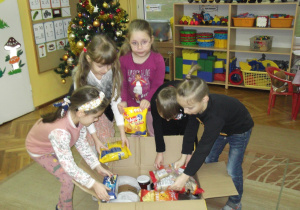 Przedszkolaki pomagają pakować produkty do paczki świątecznej.