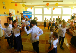 Dzieci tańczą figurę poloneza, obserwowane przez wychowawczynie pania Agnieszkę i panią Anię.