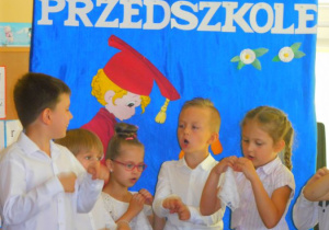 Dzieci, na tle dekoracji śpiewają piosenkę.