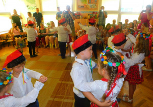 Dzieci w strojach ludowych tańczą krakowiaka.