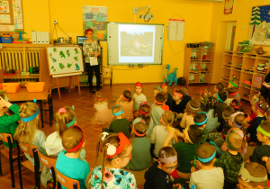 Wychowawczyni Krasnoludków prezentuje dzieciom, na tablicy multimedialnej, zdjęcia dinozaurów.