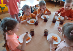 Dzieci zajadają się surówką z marchewki podaną na obiad.