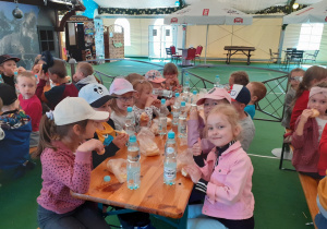 Przedszkolaki posilają się przy stolikach w hali.