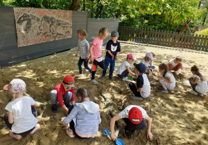 Dzieci odkopują w piasku szkielet dinozaura.