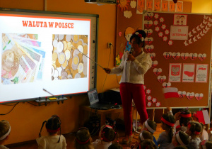 Pani Kamilka pokazuje dzieciom obowiązującą walutę w Polsce.