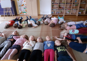 Dzieci leżą na dywanie podczas zabawy relaksacyjnej.