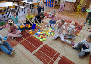 Dzieci z grupy Biedronek bawią się na dywanie nowymi zabawkami.