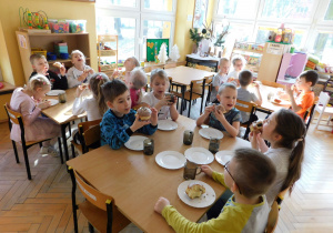 Dzieci z grupy "Krasnoludki" siedzą przy stolikach i kosztują pysznych pączków.