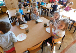 Dzieci z grupy "Misiaczki" siedzą przy stolikach i kosztują pysznych pączków.