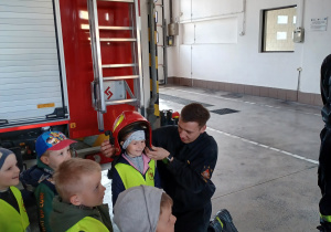 Ada z uśmiechem pokazuje się kolegom w hełmie strażackim.