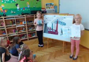 Julka i Zuzia pokazują broszurki, dzieci wyjaśniają jak dbać o czyste powietrze.