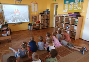 Dzieci oglądają film edukacyjny o skutkach oddychania zanieczyszczonym powietrzem.
