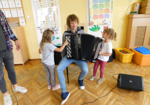Maja z grupy Biedronek rozciąga miech, a Julka z grupy Misiaczków gra melodię na białych guzikach.