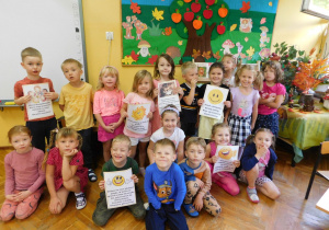Dzieci z grupy Biedronek pozują do zdjęcia pokazując uśmiechnięte na kartkach buźki.