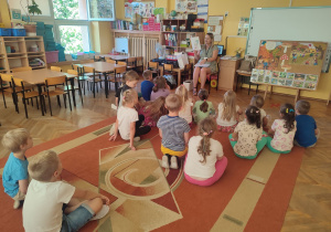Dzieci siedzą na dywanie, przed nimi Pani Patrycja pokazuje obrazek z pastą.