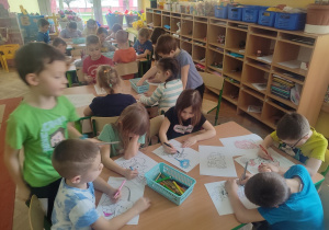 Dzieci siedzą przy stolikach i kolorują obrazki.