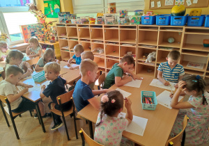 Dzieci siedzą przy stolikach i kolorują kolorowanki.