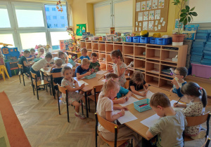 Dzieci siedzą przy stolikach i kolorują kolorowanki.