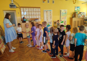 Dzieci ustawione jeden za drugim otrzymują od Olka batoniki.