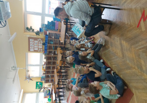 Dzieci siedzą na dywanie i słuchają bajki czytanej przez tatę Gabrysi.