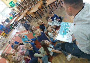 Dzieci siedzą na dywanie i słuchają bajki czytanej przez tatę Gabrysi.