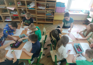 Dzieci przy stolikach kolorują kolorowanki.
