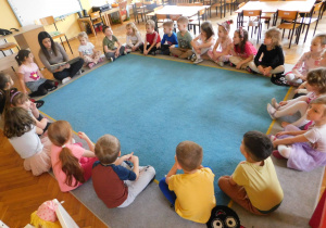 Dzieci z grupy "Biedronek" siedzą w kole na dywanie, a pani Anetka czyta dzieciom bajkę.