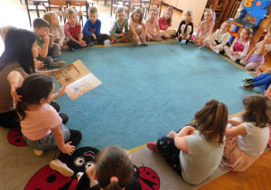 Dzieci z zainteresowaniem słuchają bajki czytanej przez panią Anetkę siedząć w kole na dywanie.