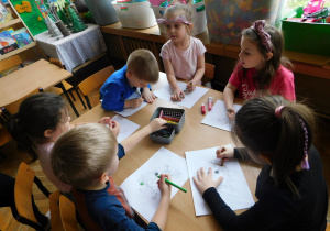 Dzieci przy stoliku kolorują obrazek sowy.