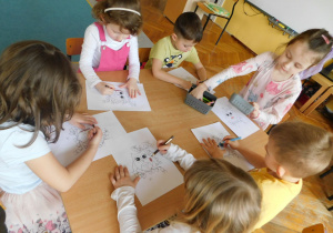 Dzieci przy stoliku kolorują obrazek sowy.