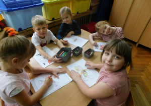 Jagoda, Nikoś, Oliwia W., Karolinka i Oliwia G. siedzą przy stoliku i kolorują malowankę Pinokia.