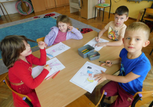Sara, Maja, Szymon i Grześ siedzą przy stoliku i kolorują malowankę Pinokia.