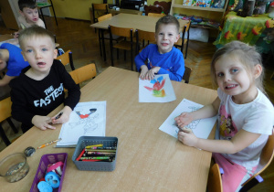 Laura, Wojtuś i Bartuś siedzą przy stoliku i kolorują malowankę Pinokia.