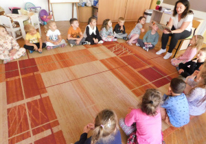 Grupa Biedronek siedzi w kole na dywanie, a pani Dominika Gajda czyta dzieciom bajkę "Dumbo".