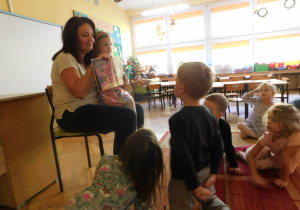 Pani Dominika trzymając na kolanach Oliwię, czyta dzieciom bajkę "Dumbo":