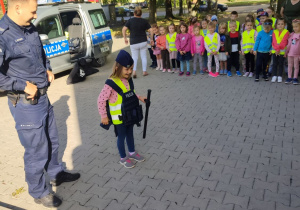 Julka ubrane w czapkę i kamizelkę kuloodporną z Panem Policjantem stoją przed dziećmi.