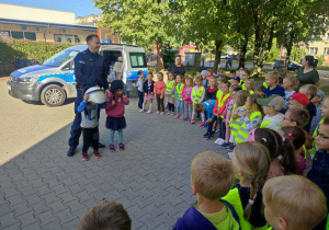 Dzieci ubrane w kaski stoja z Panem Policjantem.