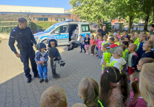1.Chłopcy w kaskach i tarczą ochronną stoją z Panem Policjantem przed dziećmi.